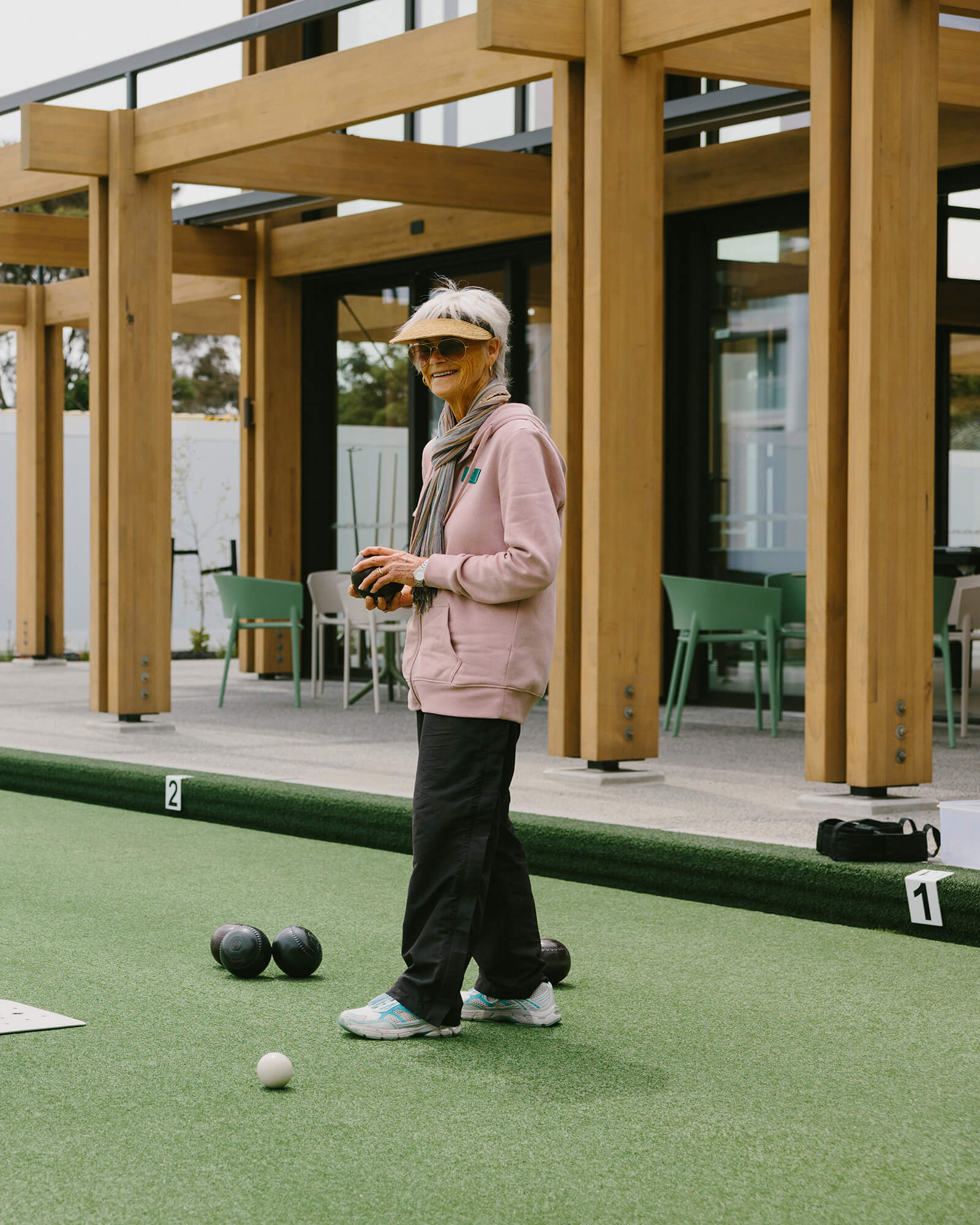 Woman wearing sun visor and glasses holds a black bowl at the end of the rink, with the club house behind.