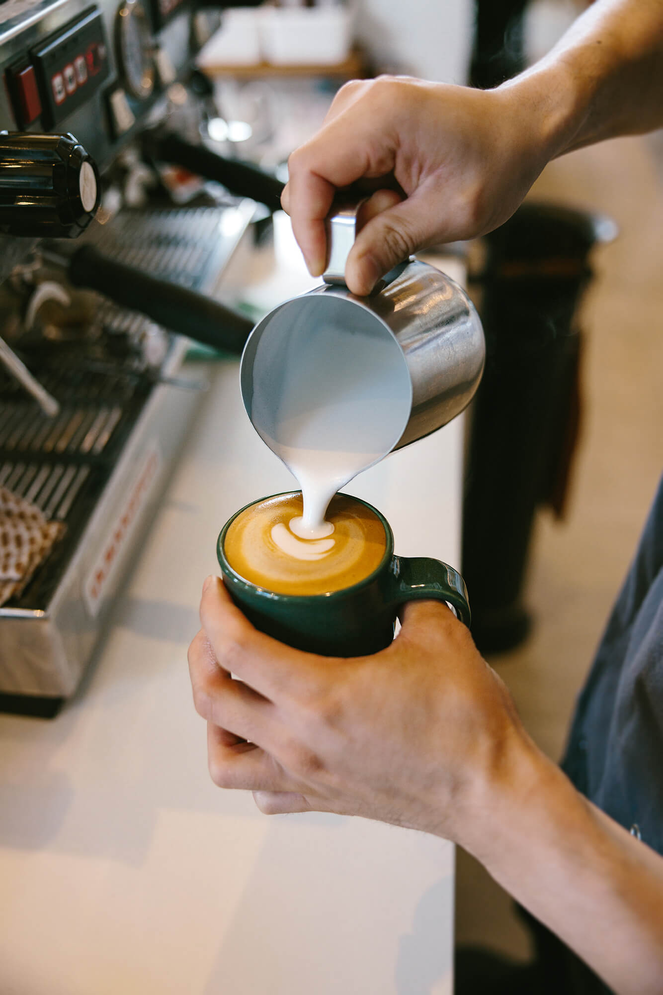 Close up of barista’s hands as freshly steamed milk is poured into a latte mug.