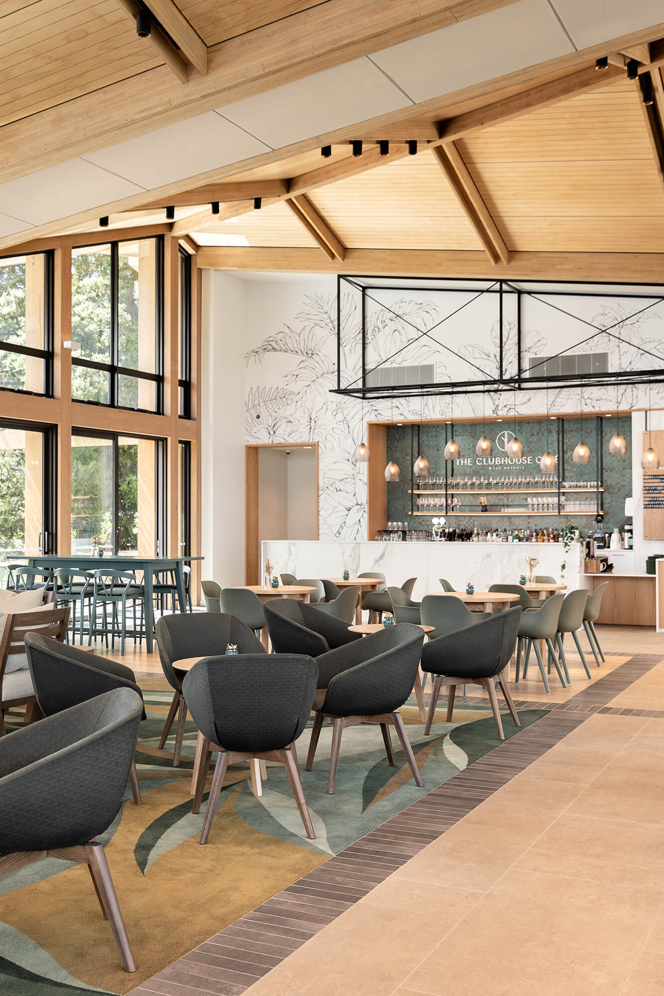 Comfortable grey fabric chairs are grouped around small wooden tables. The Clubhouse Café bar is situated on the back wall behind the tables.