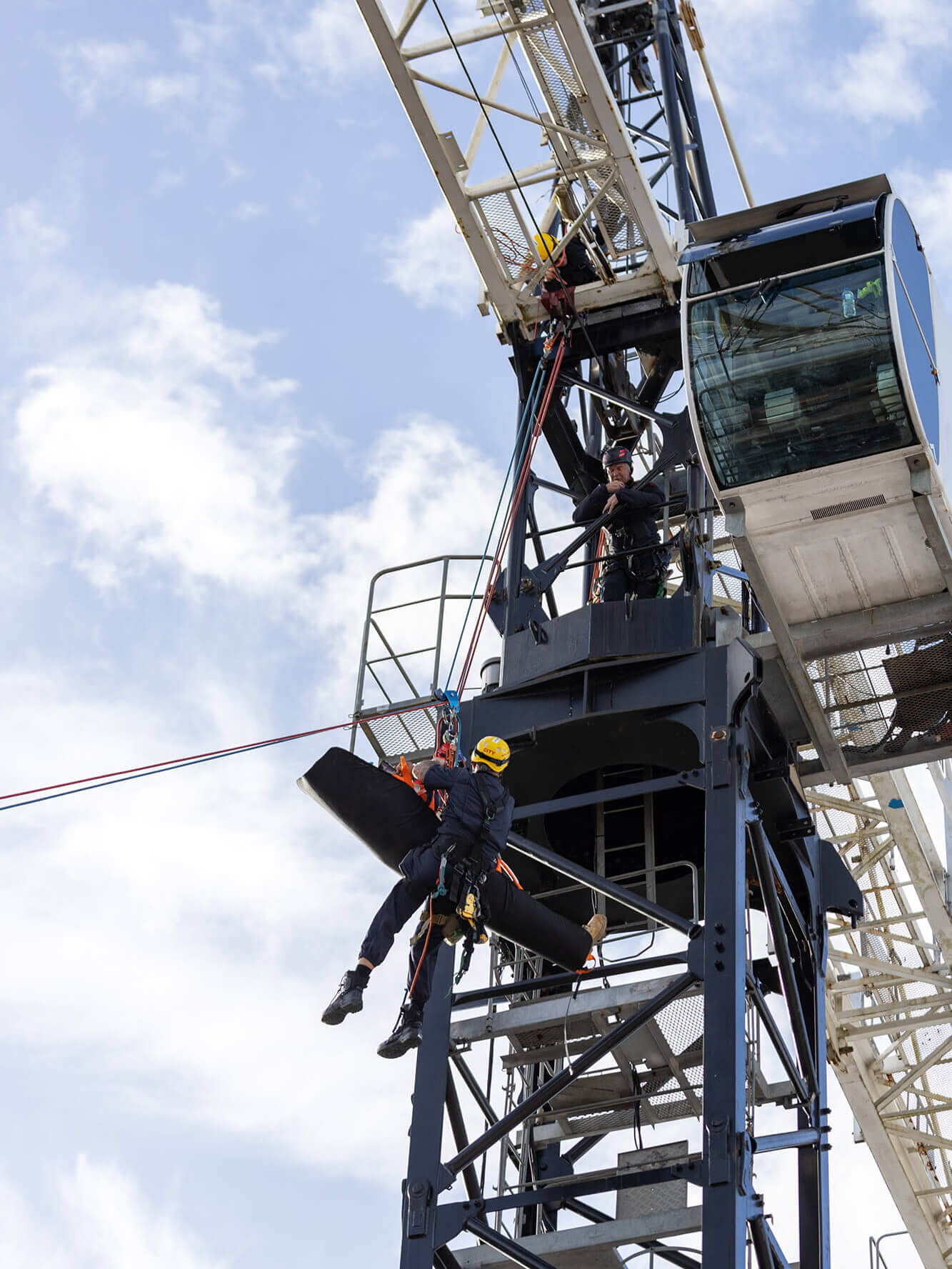 A fire brigade member abseils down from a tower crane cab with a patient suffering a medical event.