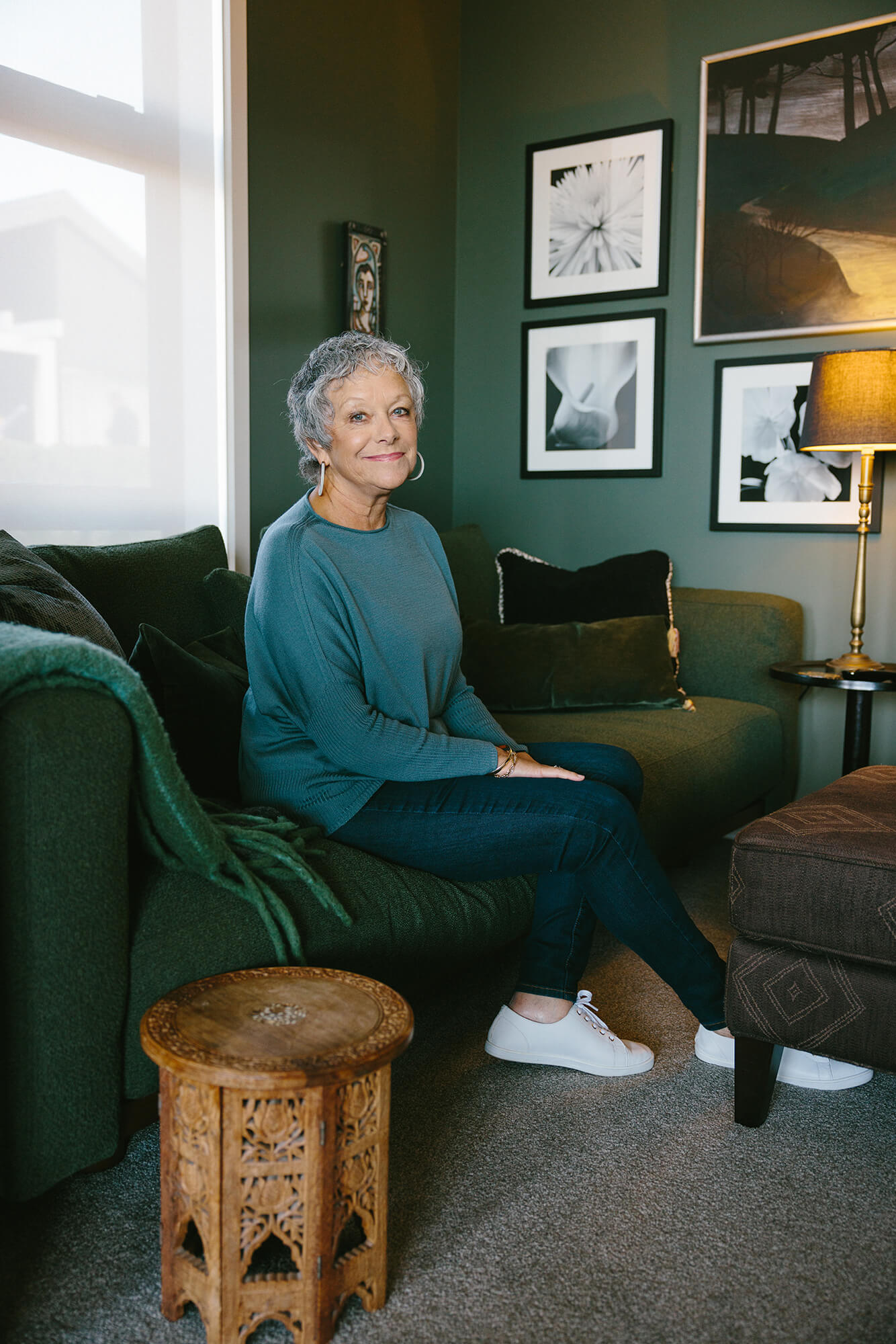 Woman sitting on green couch with black and white framed photos hung on the green wall behind her.