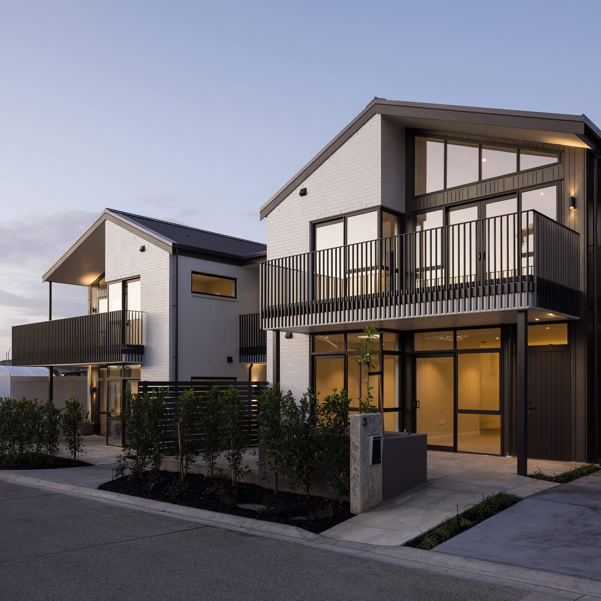 Exterior of white brick duplex villas at dusk, sun reflects off upper-level windows.