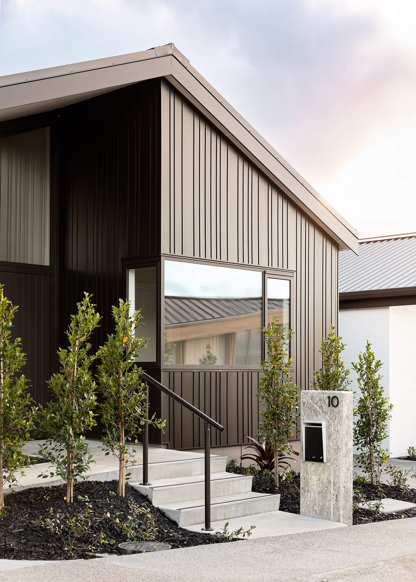 Exterior of single level villas with black vertical cladding. There are three steps up to the front door.