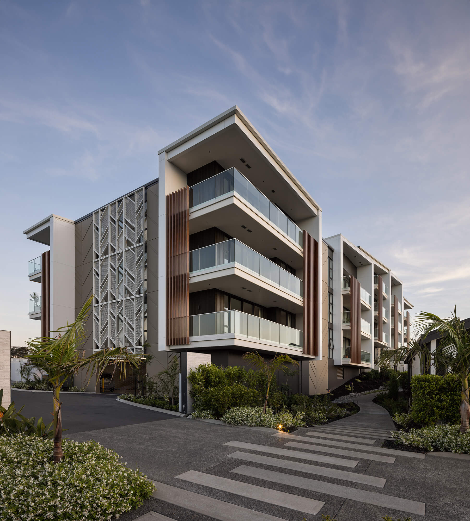 The glass railing of three sizeable balconies on corner units of the Nikau Apartment building reflect the dusk light.