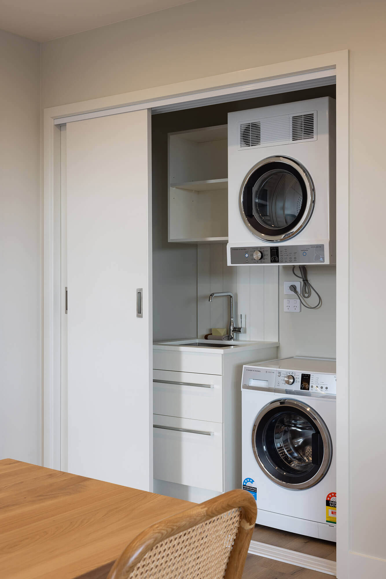 Laundry is hidden behind sliding cupboard doors. The dryer is stacked on top of the washing machine.