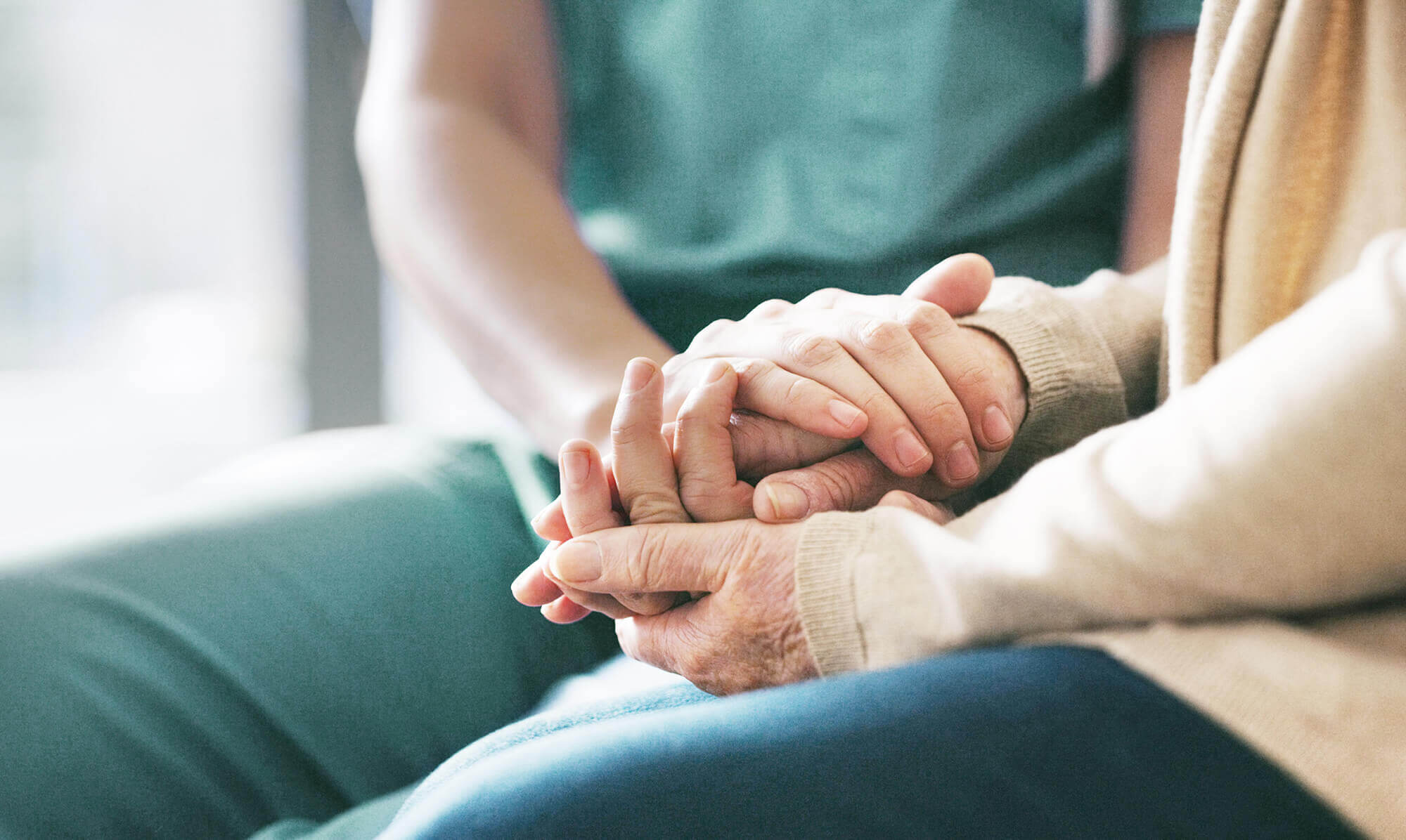 Close up of young hands resting on top of retirees hands.