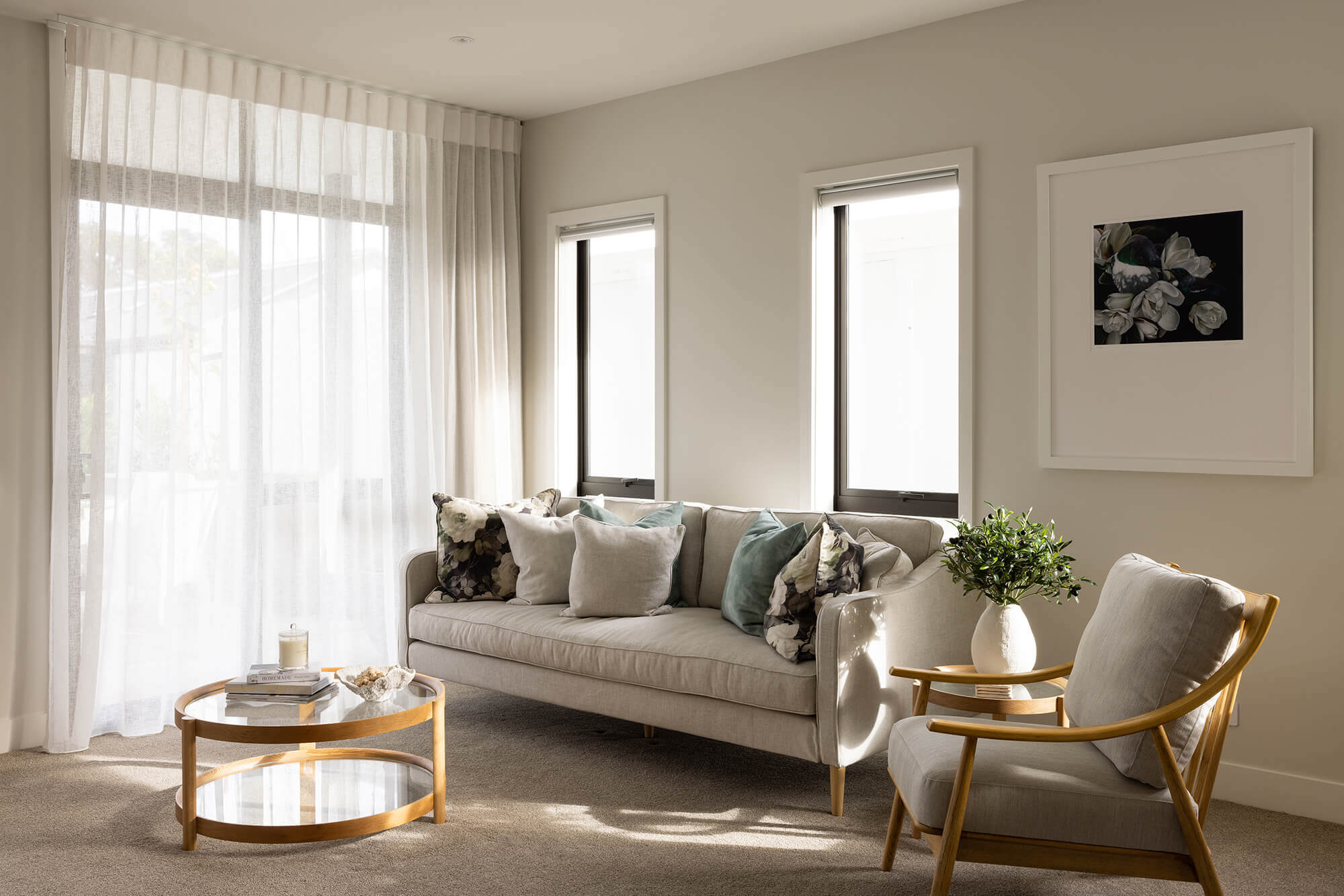 Grey couch and armchair sit in a light filled lounge area with large windows and doors.