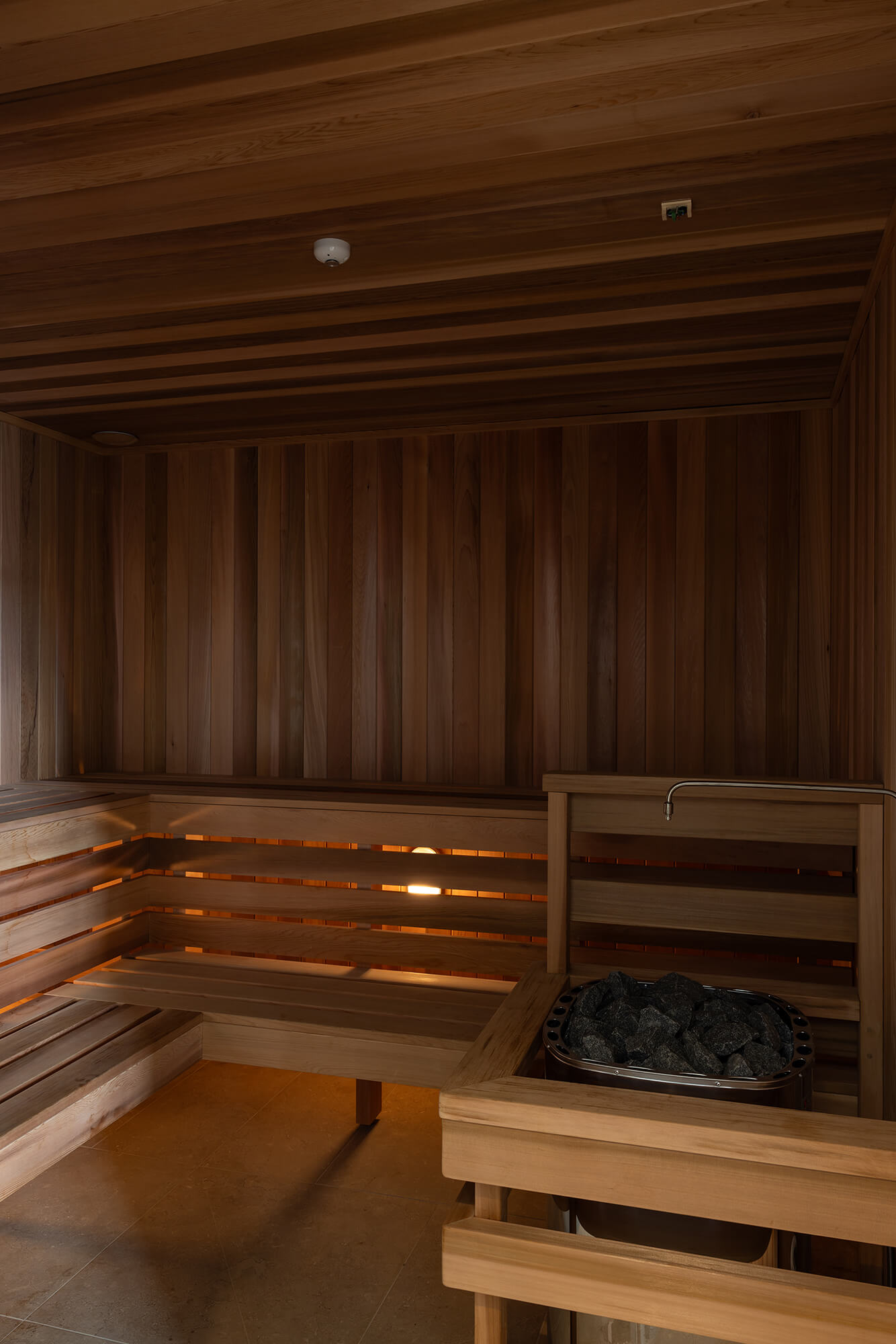 Timber lined sauna with bench seats on the left and hot steam stones on the right.