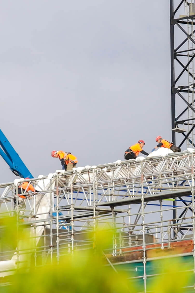 Spy-style shot of subcontractors installing roof tent fabric over Rimu building scaffolding.