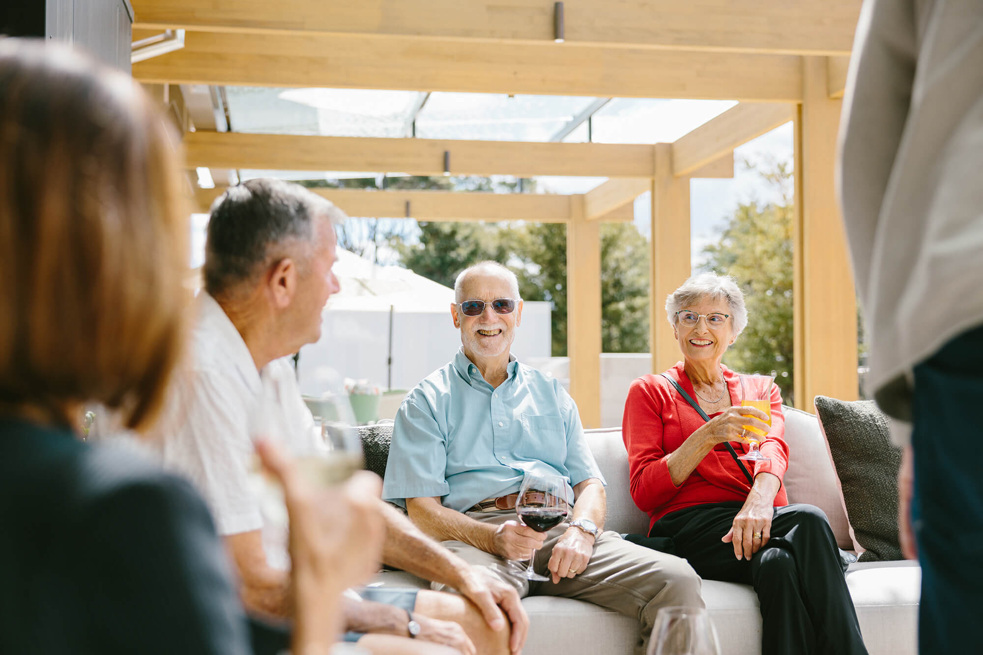 Man holding a glass of red wine smiles towards the camera with a group of retirees talking around him.