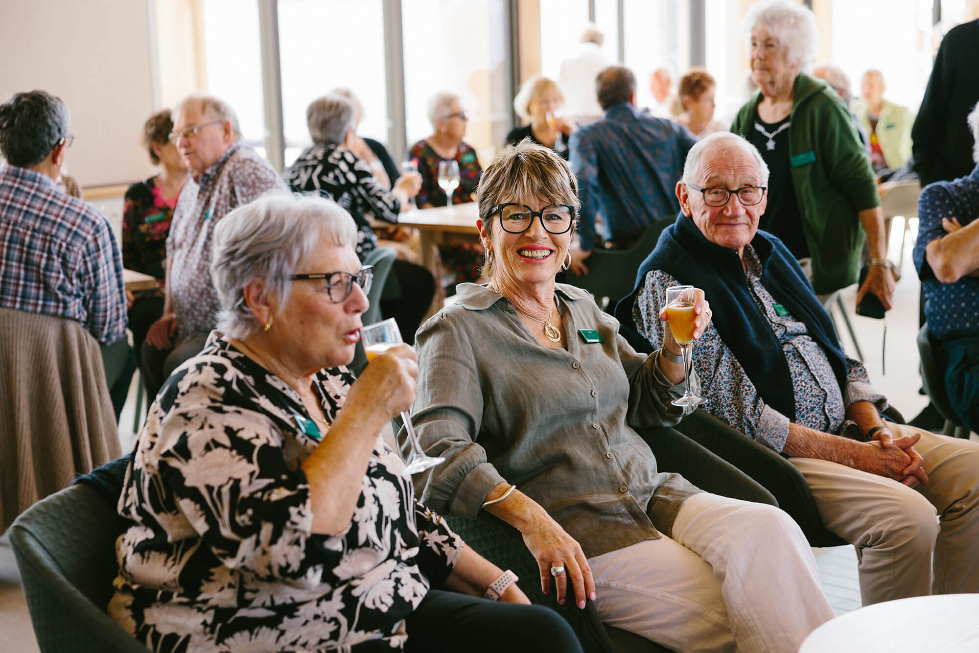 Retired woman wearing glasses smiles with a glass of bubbles in hand.