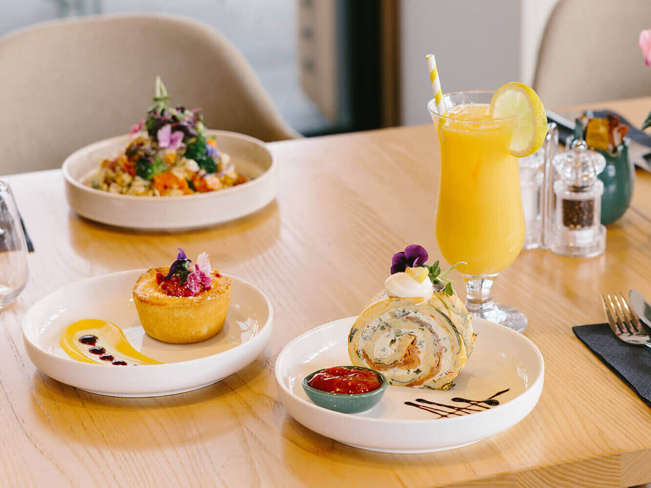 Plated cabinet food is arranged on wooden cafe table with fresh orange juice drinks.